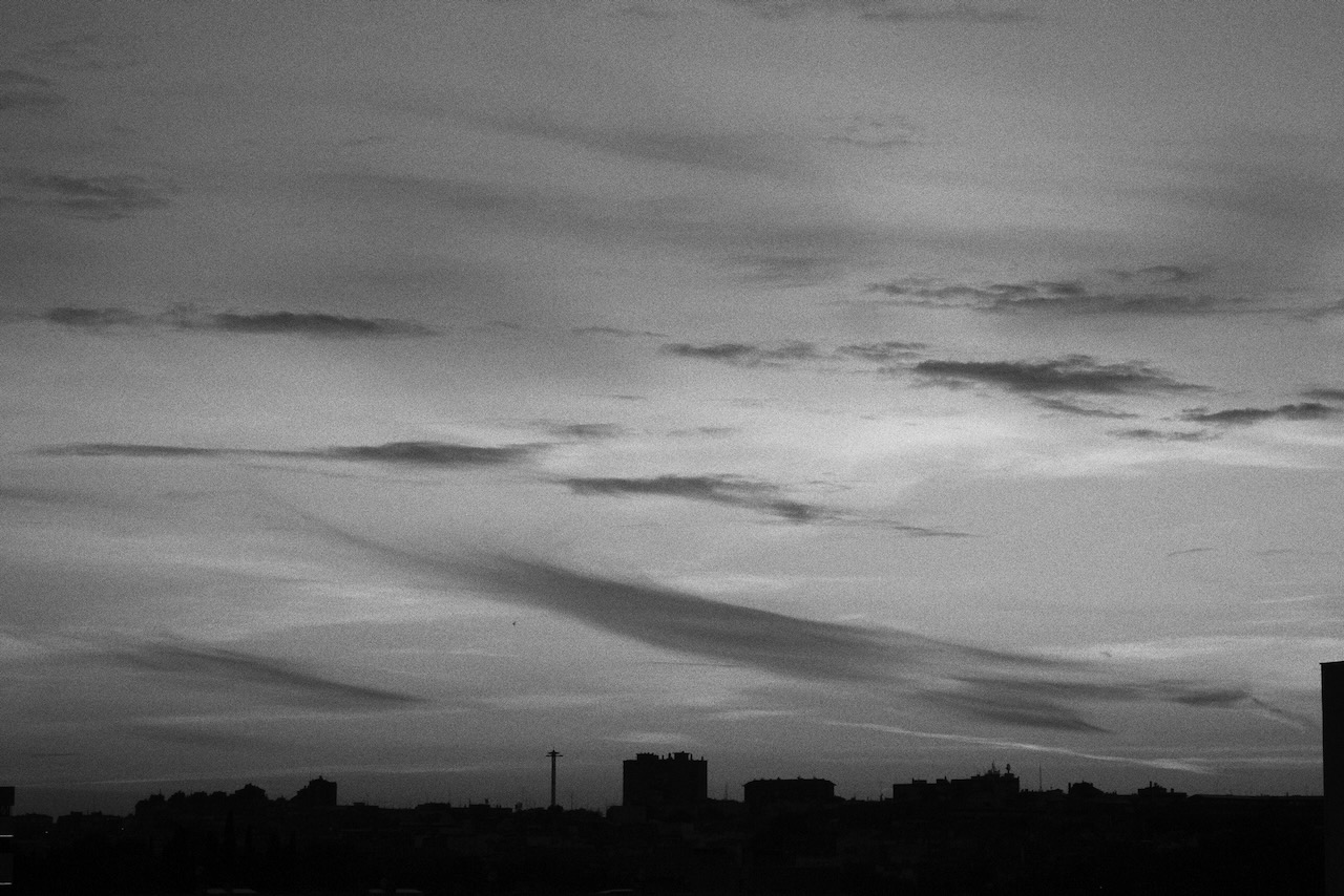 Black and white city skyline silhouetted beneath layered clouds at sunset.