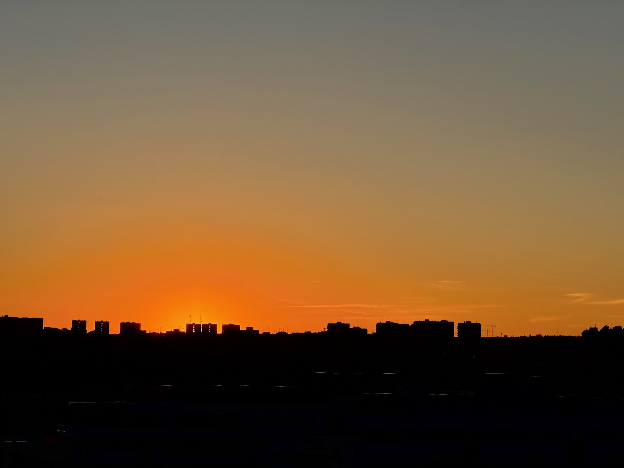 Silhouette of buildings against a vibrant orange sunset sky.