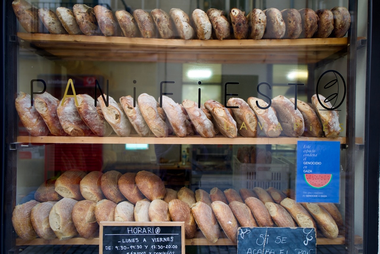 Bakery display with baguettes and loaves, open hours, and a political message.