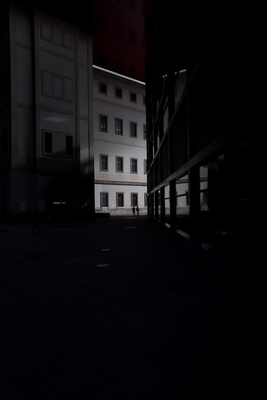 Two people walking in a dimly lit courtyard between modern buildings.