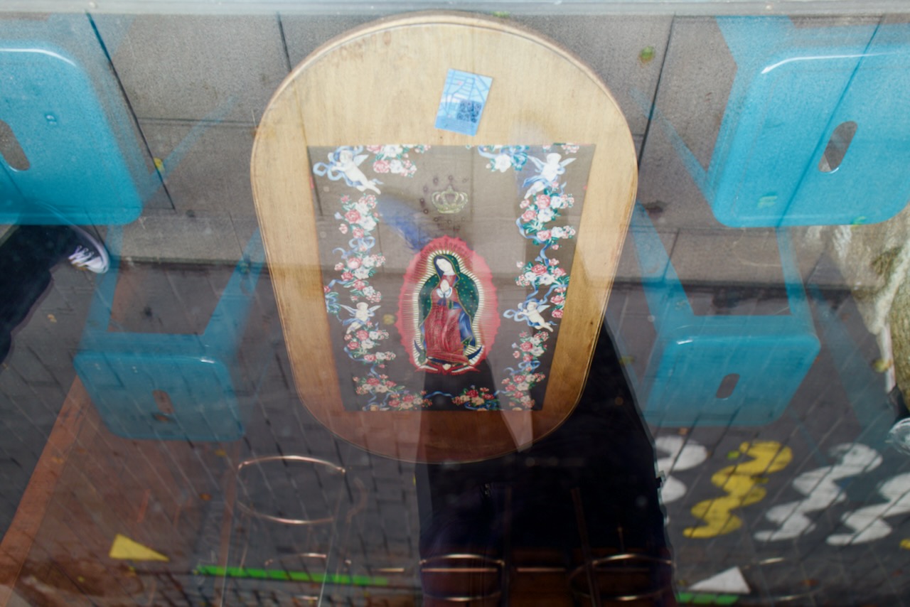 Wooden table with floral border, religious image, blue chairs, visible through glass window.